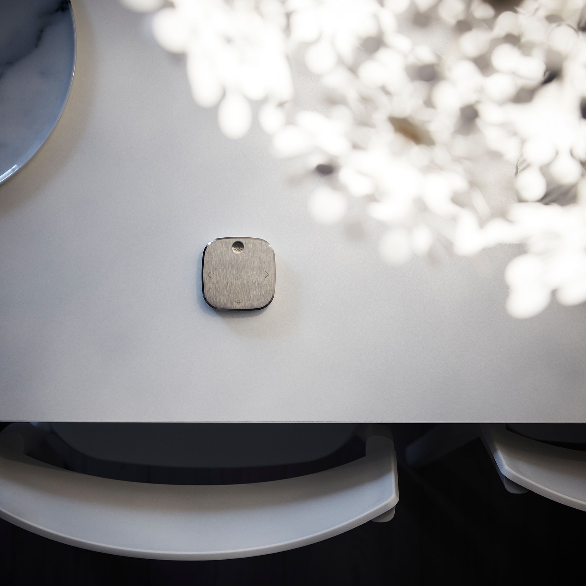 Photo from above a table focusing on the remote, a tiny white square with rounded corners and symbols indicating the 4 basic functions it has
