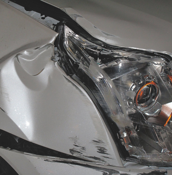 Close up photo of a smashed, wrinkled corner of a vehicle right on the zone of the front headlight.